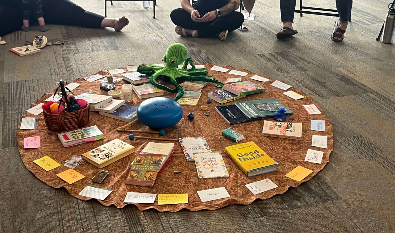 the photo shows the center of a restorative dialogue circle that is often a format used for training and discussion. Many restorative values, books, and sentimental objects of significance fill the colorful center to help ground participants during circle.